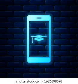 Glowing neon Graduation cap and smartphone icon. Online learning or e-learning concept icon isolated on brick wall background.  Vector Illustration