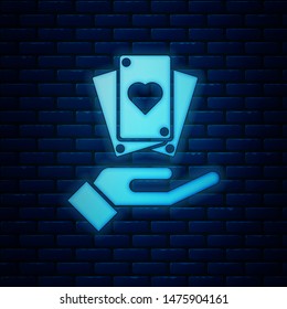 Glowing neon Hand holding playing cards icon isolated on brick wall background. Сasino game design.  Vector Illustration