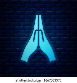 Glowing neon Hands in praying position icon isolated on brick wall background. Prayer to god with faith and hope.  Vector Illustration