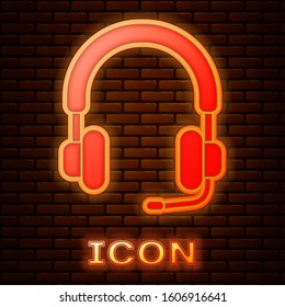 Glowing neon Headphones icon isolated on brick wall background. Earphones. Concept for listening to music, service, communication and operator.  Vector Illustration