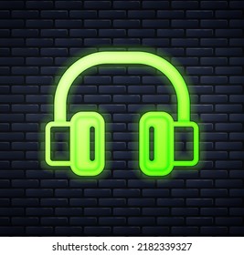 Glowing neon Headphones icon isolated on brick wall background. Earphones. Concept for listening to music, service, communication and operator.  Vector