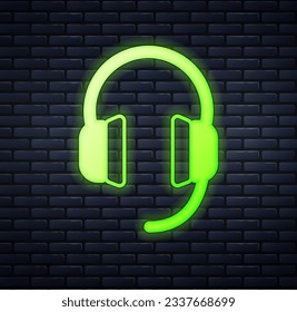 Glowing neon Headphones icon isolated on brick wall background. Earphones. Concept for listening to music, service, communication and operator.  Vector