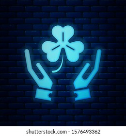 Glowing neon Human hands holding four leaf clover icon isolated on brick wall background. Happy Saint Patrick day.  Vector Illustration