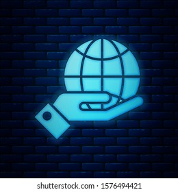 Glowing neon Human hands holding Earth globe icon isolated on brick wall background. Save earth concept.  Vector Illustration