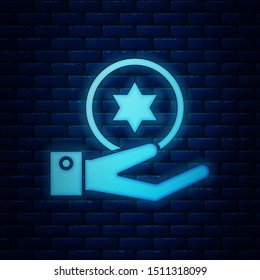 Glowing neon Jewish coin on hand icon isolated on brick wall background. Currency symbol.  Vector Illustration