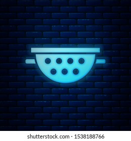 Glowing neon Kitchen colander icon isolated on brick wall background. Cooking utensil. Cutlery sign.  Vector Illustration