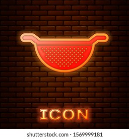 Glowing neon Kitchen colander icon isolated on brick wall background. Cooking utensil. Cutlery sign.  Vector Illustration