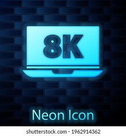 Glowing neon Laptop screen with 8k video technology icon isolated on brick wall background.  Vector