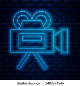 Glowing neon line Cinema camera icon isolated on brick wall background. Video camera. Movie sign. Film projector.  Vector Illustration
