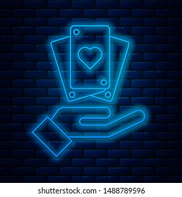 Glowing neon line Hand holding playing cards icon isolated on brick wall background. Casino game design.  Vector Illustration