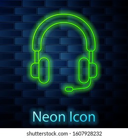 Glowing neon line Headphones icon isolated on brick wall background. Earphones. Concept for listening to music, service, communication and operator.  Vector Illustration