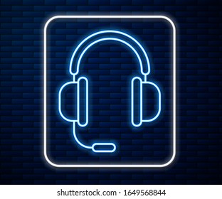 Glowing neon line Headphones with microphone icon isolated on brick wall background.  Vector Illustration