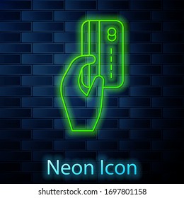 Glowing neon line Human hand holding with credit card icon isolated on brick wall background. Online payment. Pay by card. Financial operations. Vector Illustration