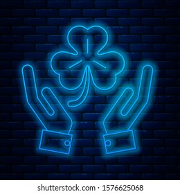 Glowing neon line Human hands holding four leaf clover icon isolated on brick wall background. Happy Saint Patrick day.  Vector Illustration