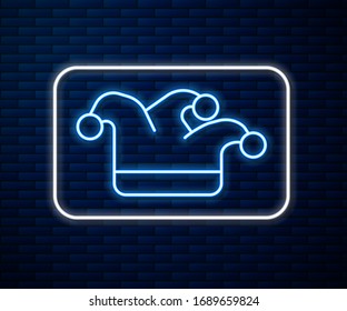 Glowing neon line Joker playing card icon isolated on brick wall background. Jester hat with bells. Casino gambling.  Vector Illustration