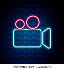 Glowing neon line Movie or Video camera icon isolated on brick wall background. Cinema camera icon. Colorful outline concept. Vector