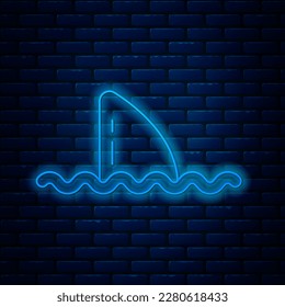 Glowing neon line Shark fin in ocean wave icon isolated on brick wall background.  Vector