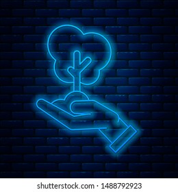 Glowing neon line Tree in hand of environmental protection icon isolated on brick wall background. Seed and seedling. Planting sapling. Ecology concept.  Vector Illustration