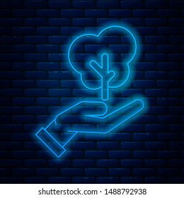 Glowing neon line Tree in hand of environmental protection icon isolated on brick wall background. Seed and seedling. Planting sapling. Ecology concept.  Vector Illustration