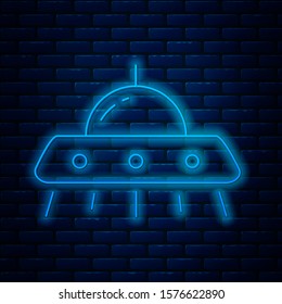 Glowing neon line UFO flying spaceship icon isolated on brick wall background. Flying saucer. Alien space ship. Futuristic unknown flying object.  Vector Illustration