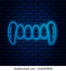 Glowing neon line Vampire teeth icon isolated on brick wall background. Happy Halloween party.  Vector Illustration