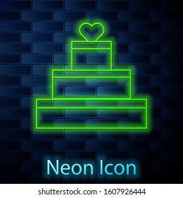 Glowing neon line Wedding cake with heart icon isolated on brick wall background. Valentines day symbol.  Vector Illustration