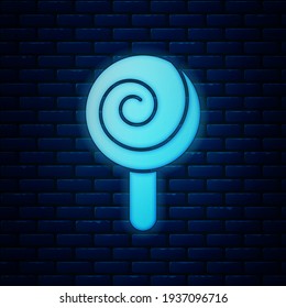 Glowing neon Lollipop icon isolated on brick wall background. Candy sign. Food, delicious symbol.  Vector