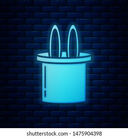 Glowing neon Magician hat and rabbit ears icon isolated on brick wall background. Magic trick. Mystery entertainment concept.  Vector Illustration