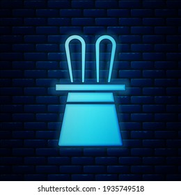 Glowing neon Magician hat and rabbit ears icon isolated on brick wall background. Magic trick. Mystery entertainment concept.  Vector