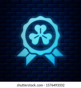 Glowing neon Medal with four leaf clover icon isolated on brick wall background. Happy Saint Patrick day.  Vector Illustration