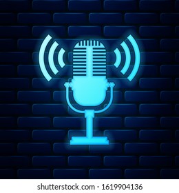 Glowing neon Microphone icon isolated on brick wall background. On air radio mic microphone. Speaker sign.  Vector Illustration