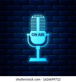 Glowing neon Microphone icon isolated on brick wall background. On air radio mic microphone. Speaker sign.  Vector Illustration