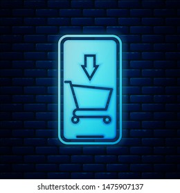 Glowing neon Mobile phone and shopping cart icon isolated on brick wall background. Online buying symbol. Supermarket basket symbol.  Vector Illustration