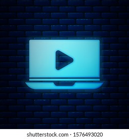 Glowing neon Online play video icon isolated on brick wall background. Laptop and film strip with play sign.  Vector Illustration