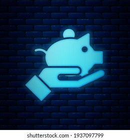 Glowing neon Piggy bank in hand icon isolated on brick wall background. Icon saving or accumulation of money, investment.  Vector