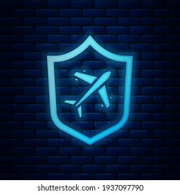 Glowing neon Plane with shield icon isolated on brick wall background. Flying airplane. Airliner insurance. Security, safety, protection, protect concept.  Vector