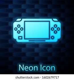 Glowing neon Portable video game console icon isolated on brick wall background. Gamepad sign. Gaming concept.  Vector Illustration