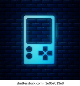 Glowing neon Portable video game console icon isolated on brick wall background. Gamepad sign. Gaming concept.  Vector Illustration