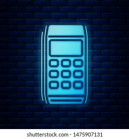 Glowing neon Pos terminal icon isolated on brick wall background. Payment terminal transaction. Pay by card.  Vector Illustration