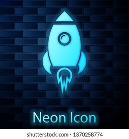 Glowing neon Rocket ship with fire icon isolated on brick wall background. Space travel. Vector Illustration