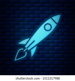Glowing neon Rocket ship with fire icon isolated on brick wall background. Space travel.  Vector Illustration