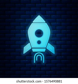 Glowing neon Rocket ship with fire icon isolated on brick wall background. Space travel.  Vector Illustration