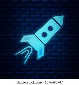 Glowing neon Rocket ship with fire icon isolated on brick wall background. Space travel.  Vector Illustration