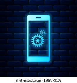 Glowing neon Setting on smartphone screen icon isolated on brick wall background. Mobile phone and gear sign. Adjusting app, set options, repair, fixing phone concepts.  Vector Illustration