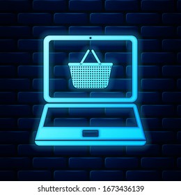 Glowing neon Shopping basket on screen laptop icon isolated on brick wall background. Concept e-commerce, e-business, online business marketing.  Vector Illustration