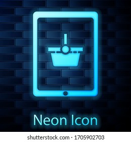 Glowing neon Shopping basket on screen tablet icon isolated on brick wall background. Concept e-commerce, e-business, online business marketing. Vector Illustration