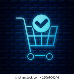 Glowing neon Shopping cart with check mark icon isolated on brick wall background. Supermarket basket with approved, confirm, done, tick, completed.  Vector Illustration