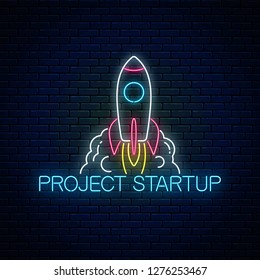 Glowing neon sign of business project startup on dark brick wall background. Business fast start symbol as a flying rocket in neon style. Vector illustration.