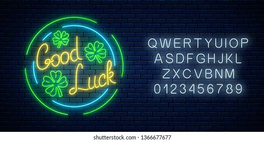 Glowing neon sign with geed luck wish and four-leaf clovers in circle frames with alphabet on dark brick wall background. Hand drawn lettering and three leaves of shamrock. Vector illustration.