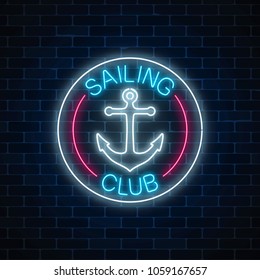 Glowing neon sign of sailing club with anchor symbol in circle frames on dark brick wall background.